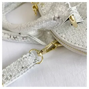 Detail of silver snake-textured shell bag showing premium golden hardware and smooth zipper