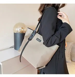 Close-up of khaki nylon tote bag with black leather handles and metal brand plate