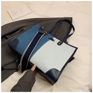 Detail of contrast denim tote bag with blue leather trim and golden metal hardware