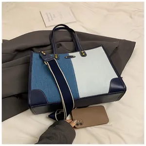 Close-up of color-block denim tote bag showing leather reinforced corners and rivet details