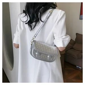 Detail of silver metallic saddle bag with intricate cross-woven flap and adjustable strap