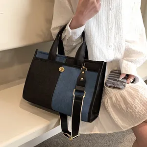 Sac fourre-tout en denim bicolore tendance avec boucle dorée porté par un mannequin