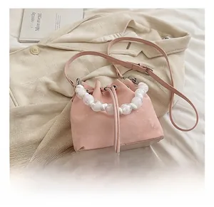 Pink drawstring bucket bag featuring white pearl bead handle and adjustable shoulder strap