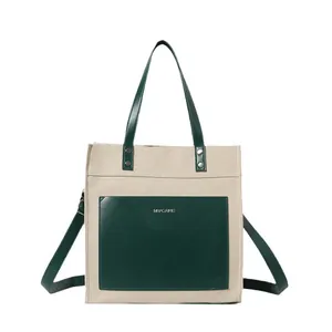 Minimalist cream canvas tote bag with deep green leather trim and large front pocket