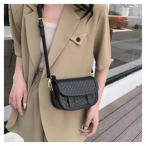 Detail of black woven leather crossbody bag with gold buckles on khaki blazer background