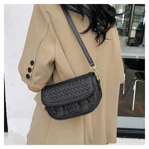 Detail of black woven leather saddle bag with gold metal buckle on female model