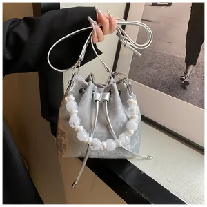 Detail of silver drawstring bucket bag featuring a large transparent beaded handle