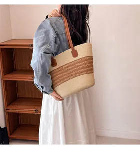 Detail of the woven texture and brown leather strap on a large straw tote bag