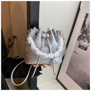 Detail of silver drawstring bucket bag with decorative white pearl chain and metal strap