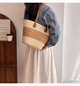 Detail of straw woven tote bag with brown leather strap worn by model in cozy setting