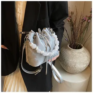 Detail of silver drawstring bucket bag with large white resin bead handle and long strap