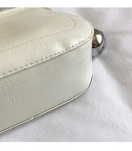 Détail d'un sac seau en cuir souple crème avec texture fine et décoration sphère argent