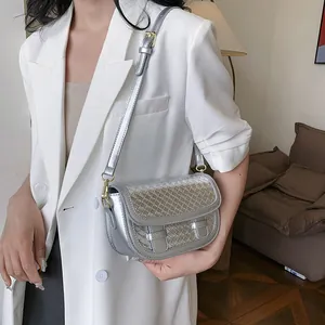 Silver metallic woven saddle bag with adjustable strap worn on a white blazer
