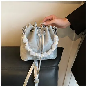 Detailed shot of silver metallic drawstring bucket bag featuring a white pearl handle
