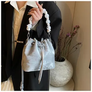 Detail of silver drawstring bucket bag with large white bead handle and metallic finish