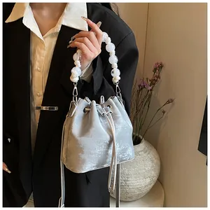 Silver bucket bag featuring textured metallic finish and white beaded handle detail