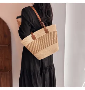 Detail of hand-woven straw tote bag featuring striped patterns and brown leather straps