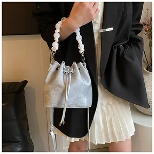 Detail of silver metallic drawstring bucket bag with pearl bead handle and slim crossbody strap
