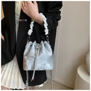 Detail of silver drawstring bucket bag with beaded handle worn with black blazer