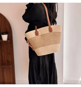 Detail of the woven straw tote bag with brown leather handles and dual-tone texture