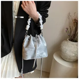 Detail of silver drawstring bucket bag with pearl handle and leather shoulder strap