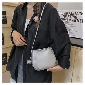 Détail du sac selle argenté avec texture métallisée, pendentif boule et bandoulière fine