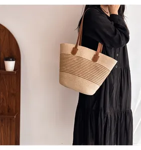 Close-up of a large straw tote bag featuring brown leather straps and woven texture