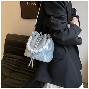 Detail of silver bucket bag with pearl handle and metal chain on a leather sofa