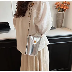 Détail du sac seau métallisé argenté avec fermoir doré et bandoulière chaîne sur bureau