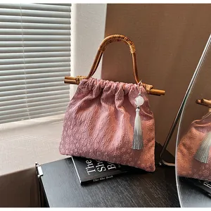 Detail van roze stoffen tas met bamboe handvaten en elegante kralenkwastje hanger