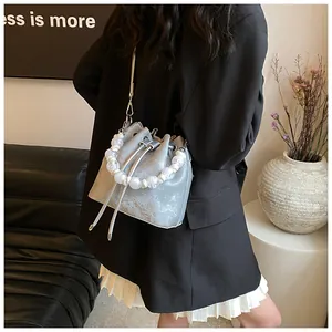 Detail of silver metallic bucket bag with pearl handle worn by model in minimalist room