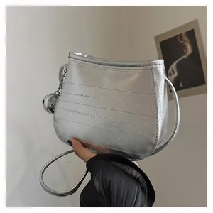 Gros plan d'un sac bandoulière argenté métallisé avec coutures et breloque boule