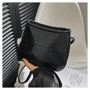 Détail du sac seau en cuir verni noir avec gaufrage horizontal et breloque argentée