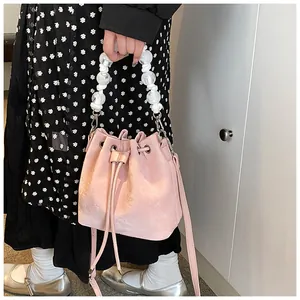 Detail of light pink drawstring bucket bag with white pearl handle and leather strap