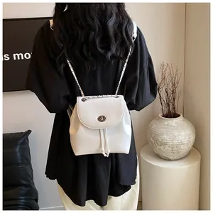 Detail eines weißen Mini-Rucksacks mit silbernem Drehverschluss und Kettenriemen an der Schulter