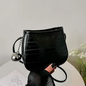 Sac bandoulière moderne en cuir verni noir avec texture côtelée et breloque boule argent