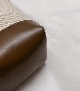 Détail macro du tissu tissé crème et des coutures en cuir marron sur un sac seau chic
