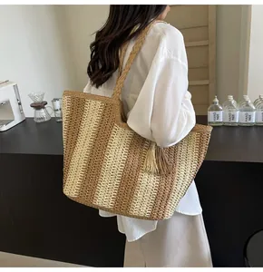 Dettaglio di una grande borsa tote in paglia con strisce kaki e manici intrecciati estivi