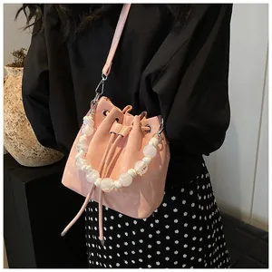 Close-up of pink bucket bag featuring drawstring closure and white beaded handle detail