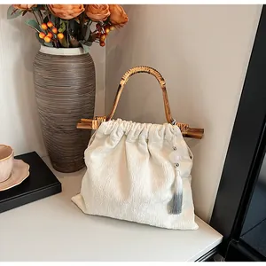 Detail van bamboe handvat en grijze kwast op een beige geplooide handtas