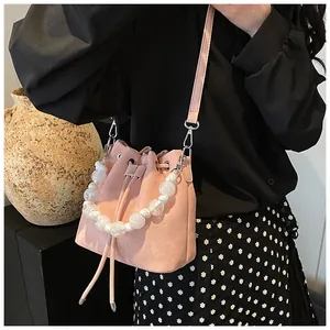 Close-up of pink drawstring bucket bag with pearl handle and long crossbody strap