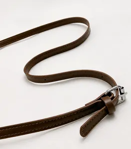 Détail d'une bandoulière en cuir marron réglable avec boucle argentée et coutures précises