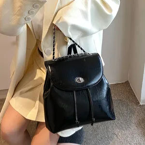 Eleganter schwarzer Mini-Rucksack mit Silberverschluss und Kettenriemen auf hellem Sakko