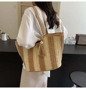 Dettaglio di borsa tote in paglia intrecciata a righe con nappa su una modella