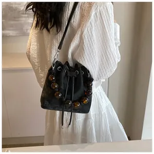 Detail of black drawstring bucket bag featuring amber resin beads and velvet texture