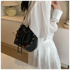 Close-up of black velvet bucket bag with amber beads on the strap shown on a model