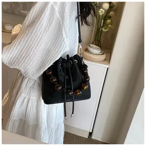 Detail of black velvet drawstring bucket bag with amber bead handle on white dress