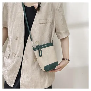 Détail du sac seau en toile et cuir vert avec logo MYCARE porté par un mannequin