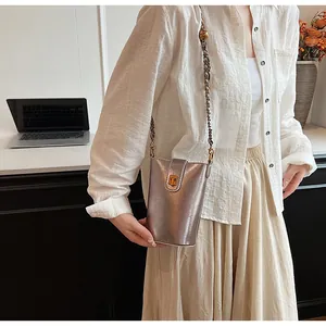 Détail d'un sac seau métallisé avec fermoir doré et bandoulière chaîne sur modèle