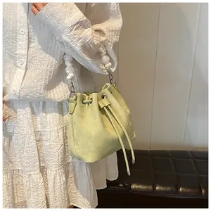 Detail view of light green drawstring bucket bag with decorative white pearl handle strap